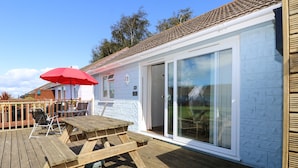 A wooden deck with a table and chairs, a red umbrella, and a sliding glass door leading to a covered patio area.