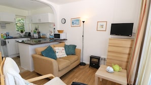 A compact living space with a kitchenette, a sofa, a chair, a small table, and a television.