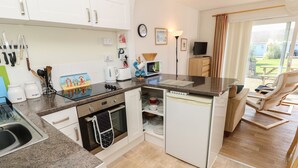 A compact kitchen with a stove, oven, and refrigerator, a dining area with a table and chairs, and a view of the outdoors through a window.