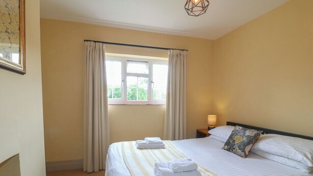 A hotel room with a bed, a nightstand, a lamp, a window with curtains, and a painting on the wall.