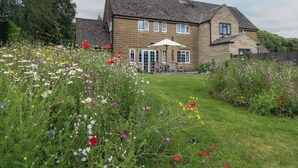 Ein zweistöckiges Steinhaus mit Garten-Terrasse, umgeben von verschiedenen Wildblumen.
