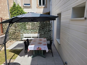 Une terrasse avec une table et des chaises, un banc blanc et un grand parasol.
