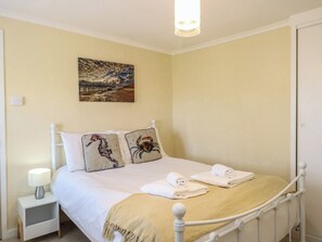 A neatly made bed with pillows, a bedside lamp, and a painting on the wall. - Cobbler's Cottage (Norwich)