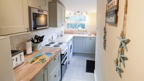 A compact kitchen with a microwave, stove, and sink. There is a window providing natural light and a view of greenery outside.
