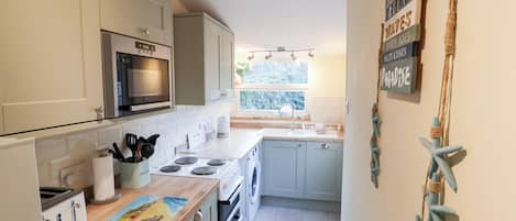 A compact kitchen with a microwave, stove, and sink. There is a window providing natural light and a view of greenery outside.