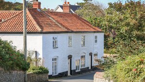 A white building with a red-tiled roof, a stone wall, and a narrow road leading to it.