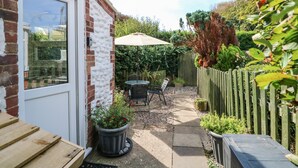 A brick house with a patio, a wooden fence, and a garden with potted plants.