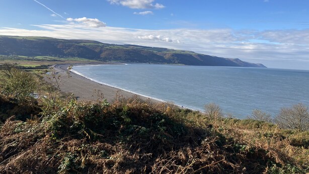 Un paysage côtier avec une plage, des collines douces et un ciel dégagé.