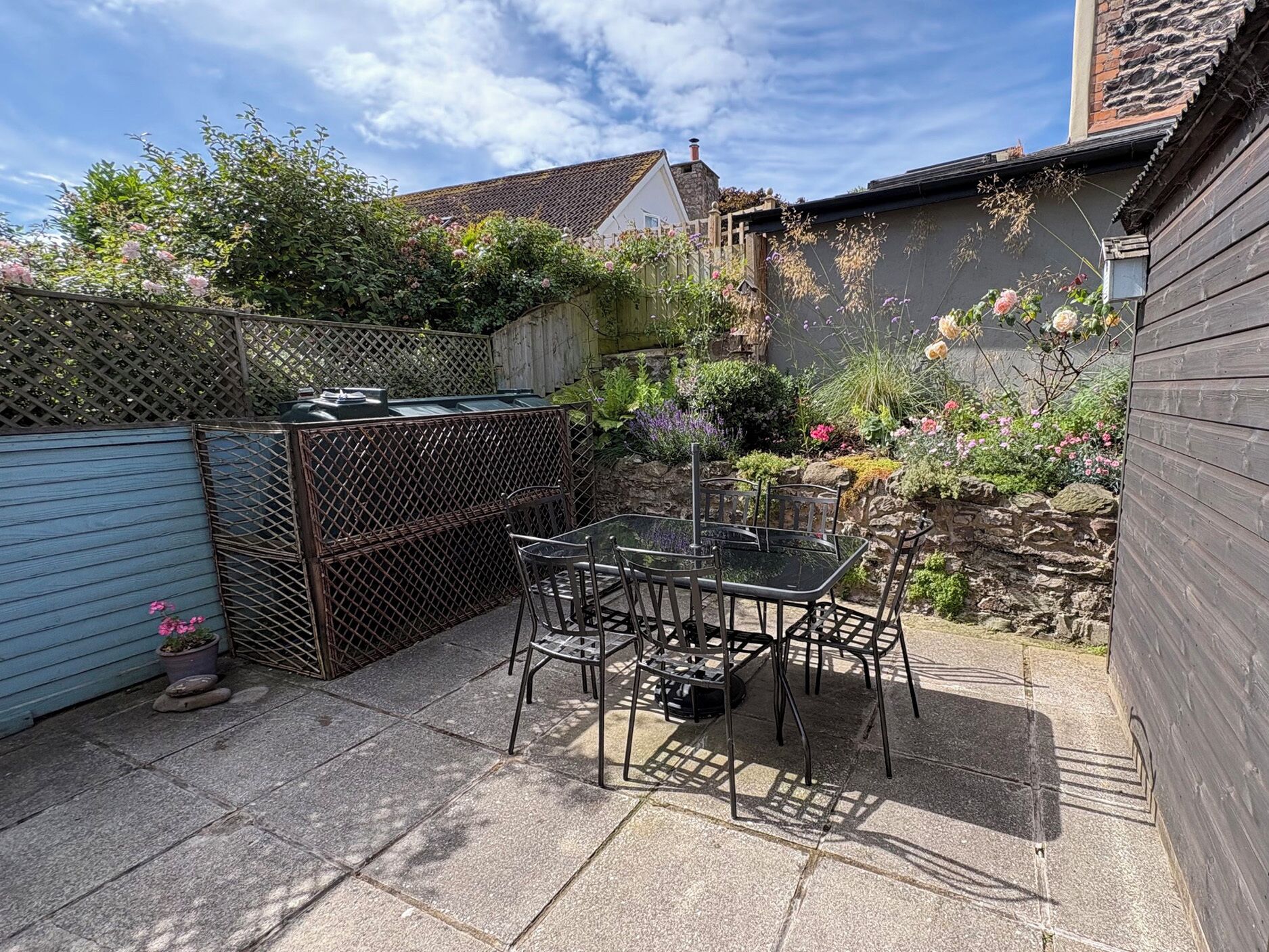 Une terrasse avec une table et des chaises, entourée d’un mur de pierre et agrémentée de différentes plantes.