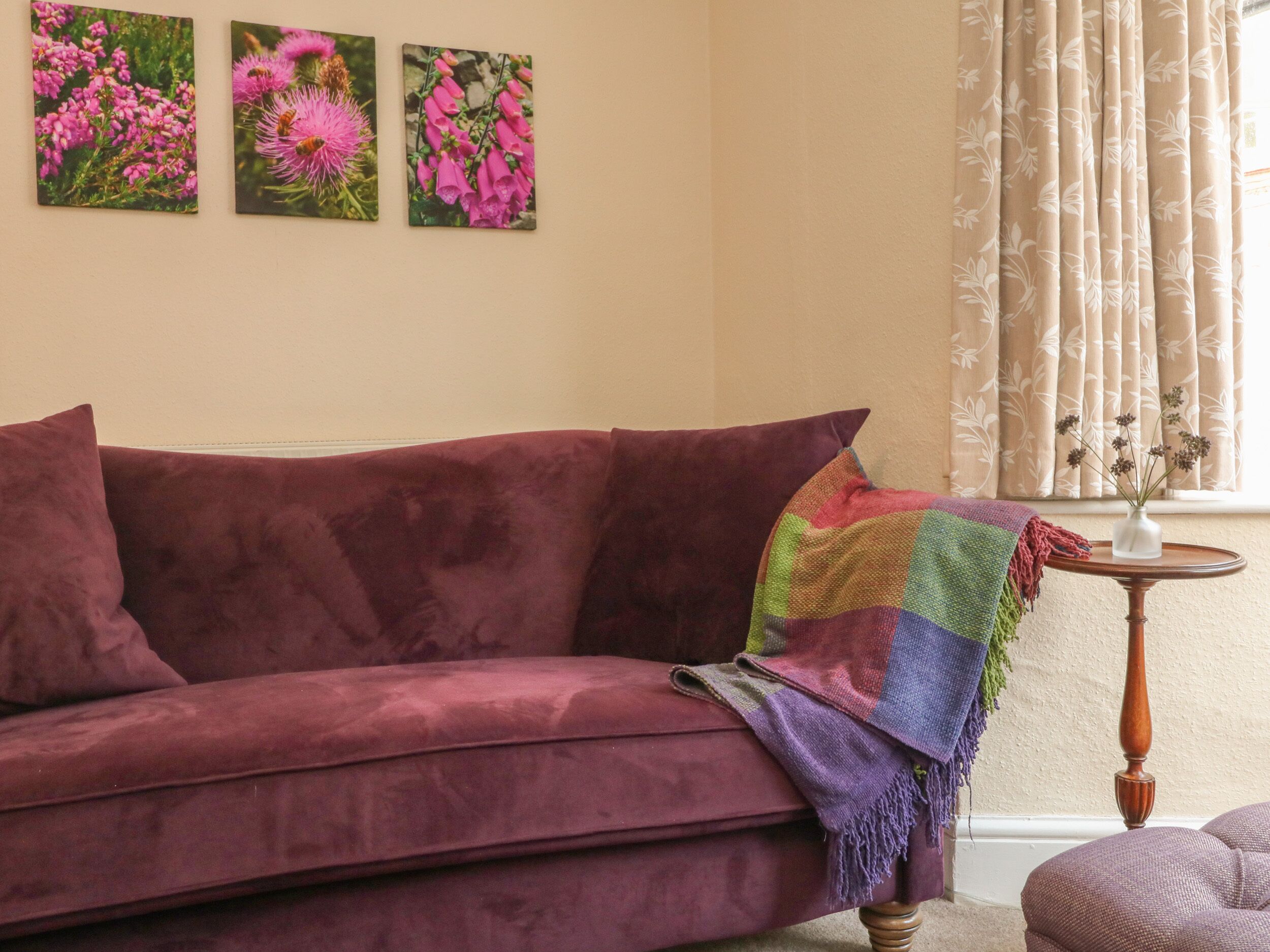 A living room with a purple sofa, a colorful throw blanket, and three framed floral paintings on the wall.