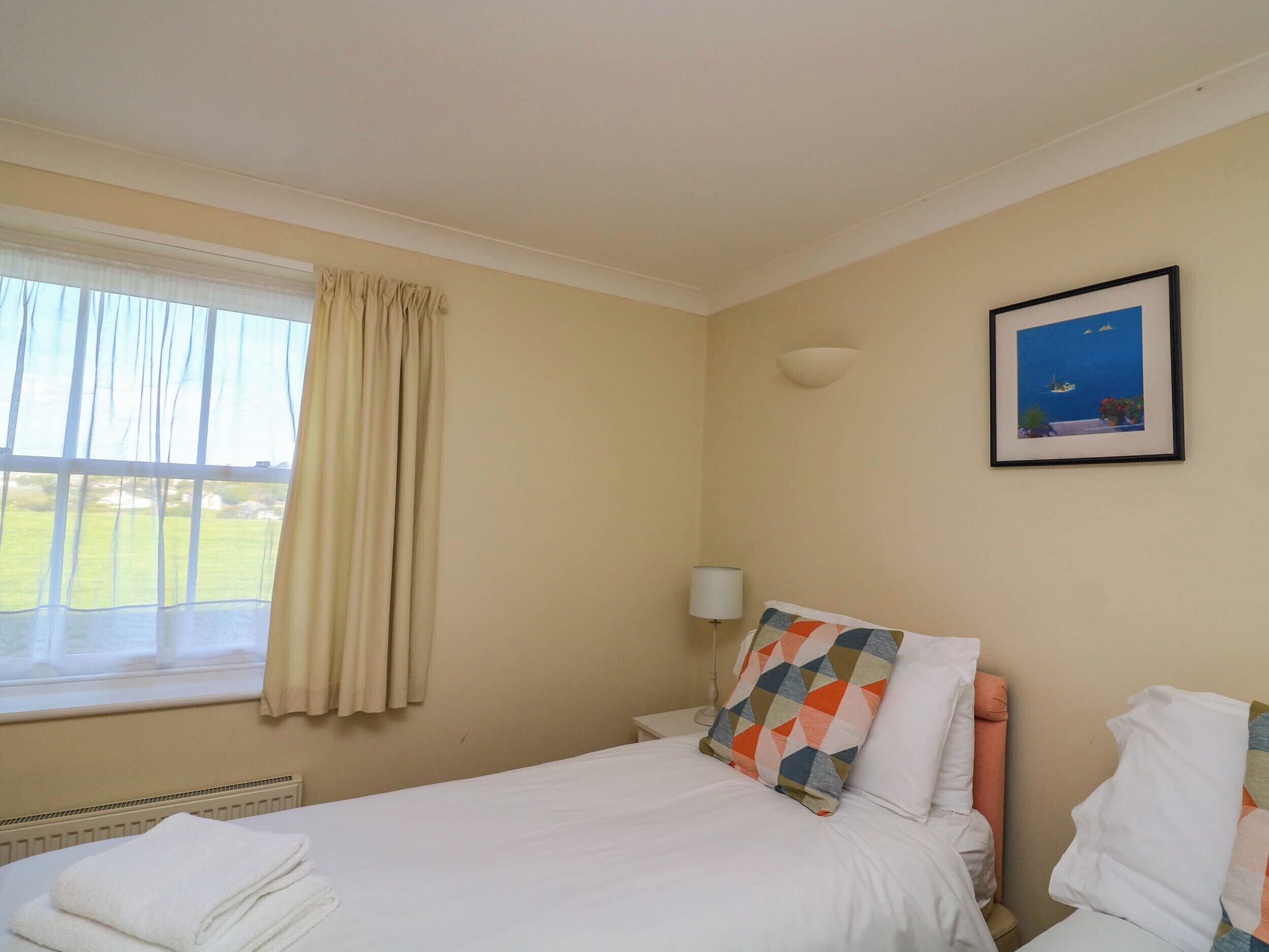 A hotel room with a bed, a window with curtains, a wall-mounted lamp, and a framed picture.