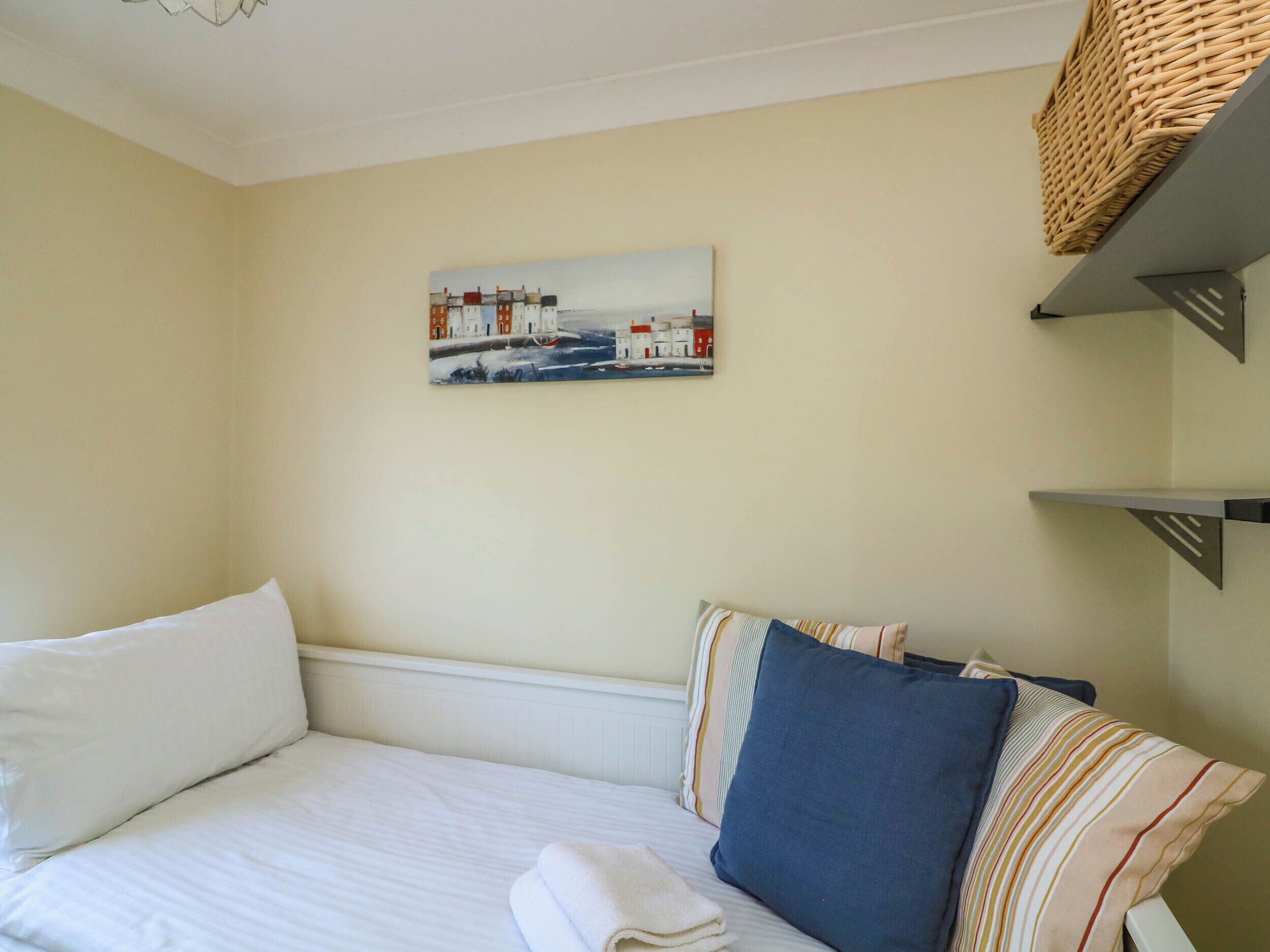 A neatly arranged bedroom with a bed, pillows, a painting, and shelves.