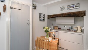 Een compacte keuken met een houten eettafel, een witte deur en een rustieke plafondbalk.