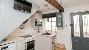Een kleine keuken met witte kasten, een inbouwoven, een magnetron en een raam met uitzicht.