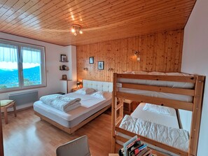 Een kamer met een stapelbed, een eenpersoonsbed, een raam met uitzicht, houten wanden en een plafond met houten balken.