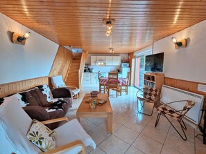Un salon chaleureux avec un canapé, une table basse et un coin repas avec des chaises. Un escalier mène à une cuisine et à un autre coin repas.