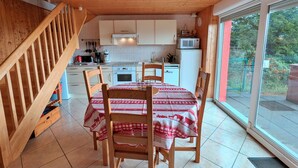 A kitchen with wooden cabinets, a dining table with chairs, and a view through a glass door. - Independent house with garden, terrace and fireplace in Saulxures-sur-Moselotte (Saulxures-sur-Moselotte)