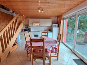 Een keuken met houten kastjes, een eettafel met stoelen en uitzicht door een glazen deur.