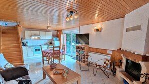 A cozy living area with a fireplace, a dining table, and a kitchen in the background. - Independent house with garden, terrace and fireplace in Saulxures-sur-Moselotte (Saulxures-sur-Moselotte)