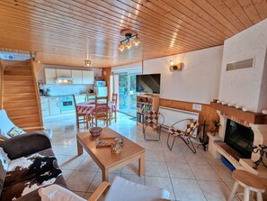 Een gezellige woonkamer met een open haard, een eethoek met een tafel en stoelen, en een keuken op de achtergrond.