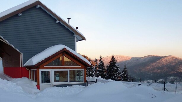 A house with a sloped roof covered in snow, a wooden cabin attached, and a mountainous backdrop. - Independent house with garden, terrace and fireplace in Saulxures-sur-Moselotte (Saulxures-sur-Moselotte)
