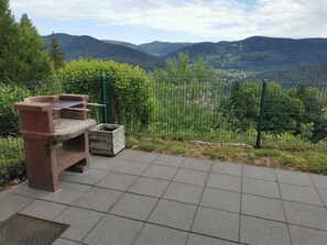 Un espace extérieur aménagé avec des sièges, un barbecue, une poubelle et une vue sur un paysage montagneux.
