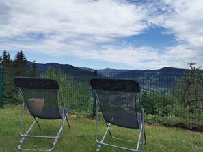 Duas cadeiras de metal com encosto em tela, voltadas para uma paisagem montanhosa, vistas através de uma cerca de arame.