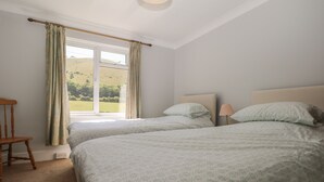 A bedroom with two beds, a wooden chair, a window with curtains, and a lamp. - 1 Paythorne Farm Cottages (Henfield)
