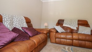 A living room with two brown leather sofas, a patterned throw blanket, and a lamp on a side table. - 1 Paythorne Farm Cottages (Henfield)