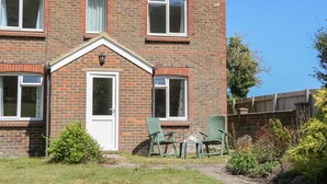 A two-story brick house with a front door, two windows on the ground floor, and a small garden area with a table and chairs. - 1 Paythorne Farm Cottages (Henfield)