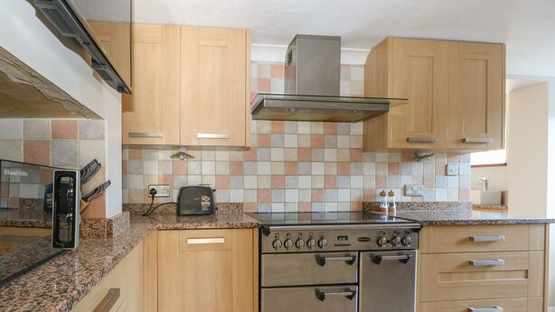 A kitchen with wooden cabinets, a stainless steel stove, and a tiled backsplash. - 1 Paythorne Farm Cottages (Henfield)