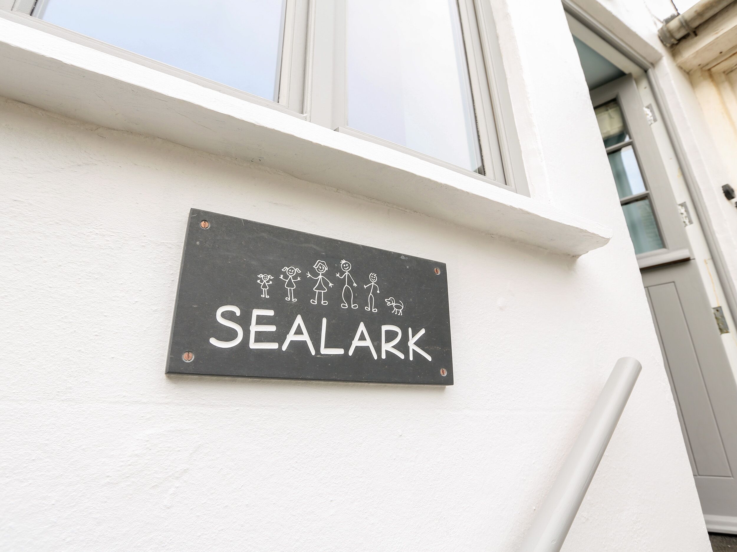 A sign on a building wall that reads "SEALARK" with a simple line drawing of people and a dog.