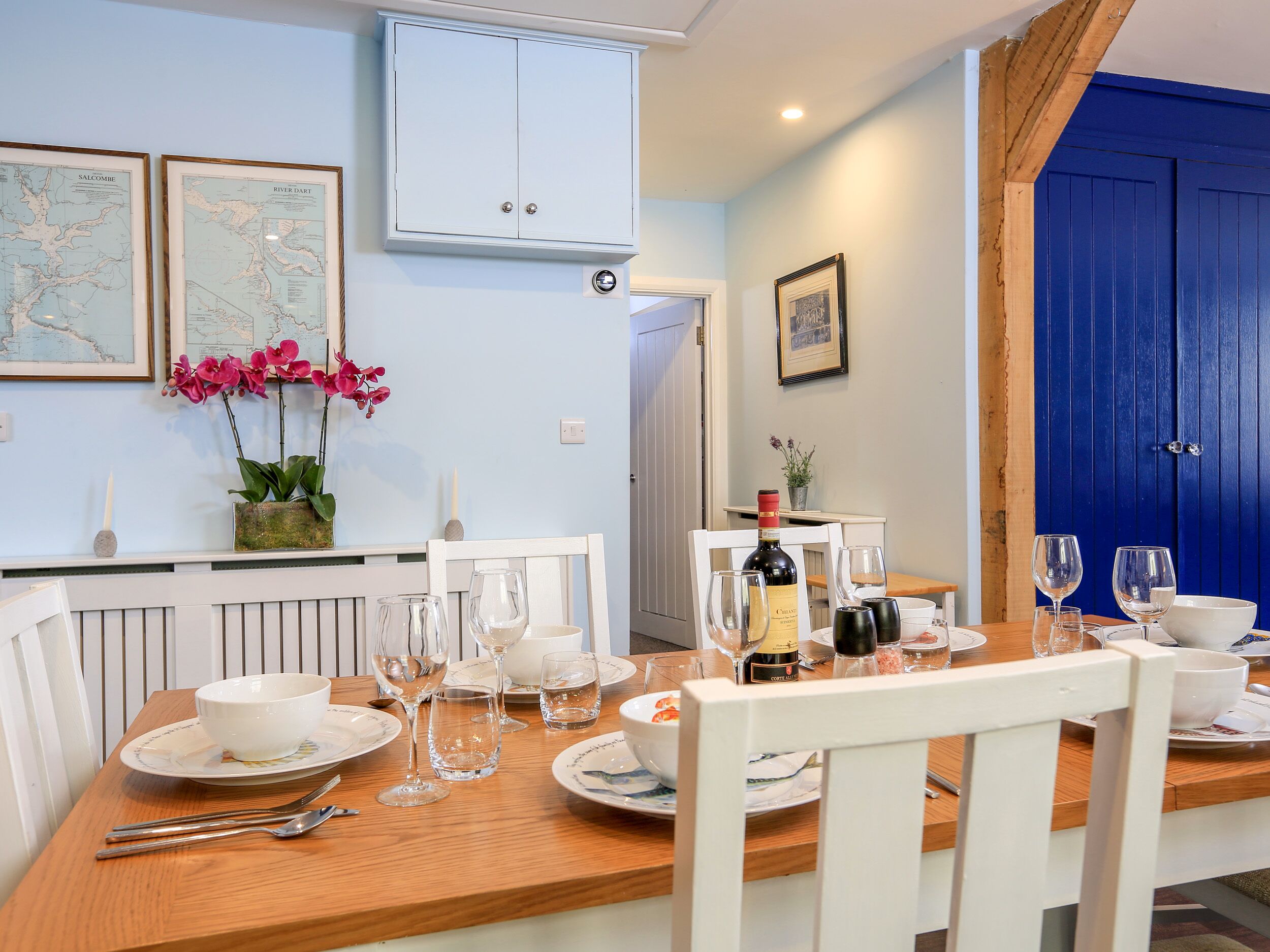 A dining area with a wooden table set for a meal, white chairs, and a blue door in the background.