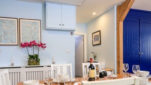 Un coin repas avec une table en bois dressée pour un repas, des chaises blanches et une porte bleue en arrière-plan.