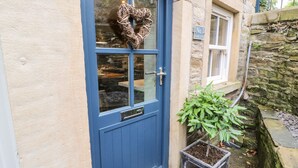 A blue door with a heart-shaped decoration, a small potted plant, and a stone wall. - 1 Oakleys (Holmfirth)