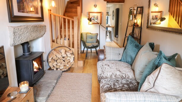 A cozy living room with a fireplace, a sofa, a chair, and a staircase leading to another room. - 1 Oakleys (Holmfirth)