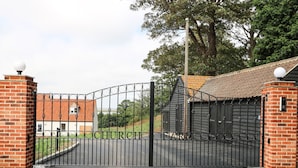 A gated entrance with a metal gate, brick walls, and a building with a tiled roof. - Waveney View Cottage (Great Yarmouth)