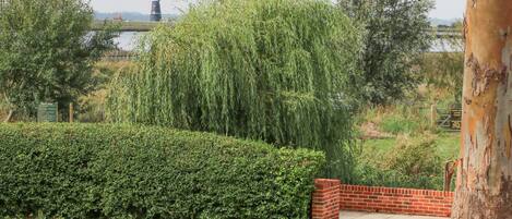 A landscaped garden with a neatly trimmed hedge, a brick bench, and a large tree.