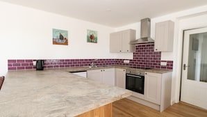 A modern kitchen with a marble countertop, wooden cabinets, and a built-in oven. - Waveney View Cottage (Great Yarmouth)