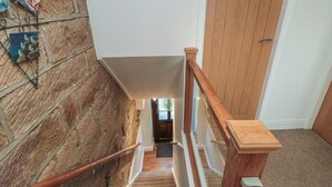 Un escalier en bois, doté d’une rampe, mène à une pièce qui possède une porte et un interrupteur sur le mur.
