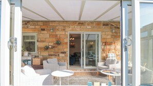 Un espace patio accueillant, doté de meubles en osier, d’une petite table et d’une porte vitrée donnant sur un espace intérieur.