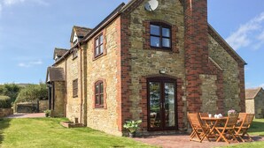 A stone house with a brick chimney, a large glass door, and a patio with wooden furniture. - Wilstone Cottage (Church Stretton)