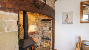 A stone fireplace with a black stove, a wooden ceiling beam, and a painting of a rabbit on the wall. - Wilstone Cottage (Church Stretton)