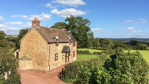 A stone building with a sloped roof, a chimney, and a small attached structure. - Wilstone Cottage (Church Stretton)