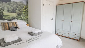A neatly made bed with a pillow, a folded towel, and a blanket with text. There is a wardrobe with wooden handles and a door with a black handle. - Town Head Cottage (Skipton)
