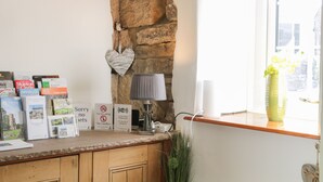 A stone wall, a window with a view, a lamp, and various informational cards on a counter. - Town Head Cottage (Skipton)