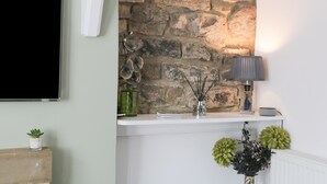 A modern living room with a stone wall, a flat-screen TV, a lamp, and decorative plants. - Town Head Cottage (Skipton)