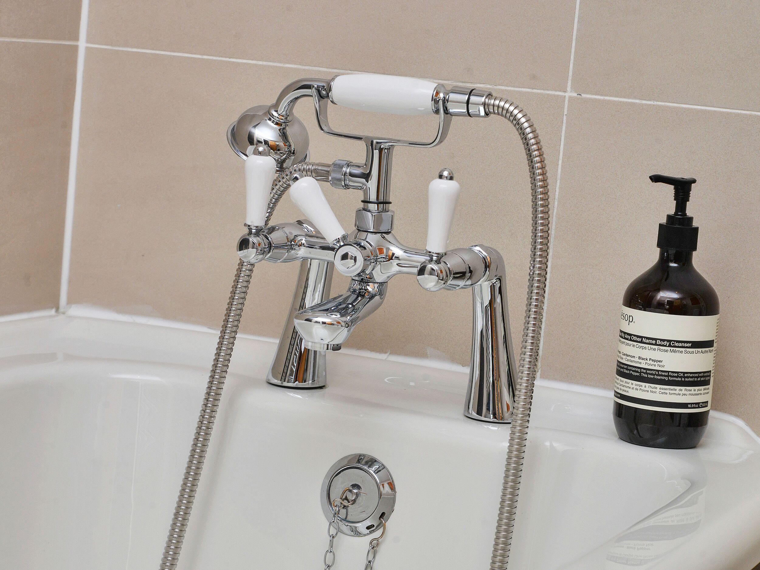 A bathroom with a chrome faucet, a showerhead, and a bottle of body cleanser.