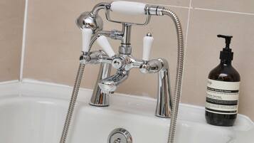 A bathroom with a chrome faucet, a showerhead, and a bottle of body cleanser.