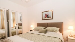 A bedroom with a large bed, a mirror, two bedside lamps, a framed picture on the wall, and a chandelier. - 2B Cavendish Villas (Buxton)
